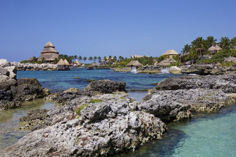 Rocky Mexican Caribbean coastline with clear water and palm-roofed huts