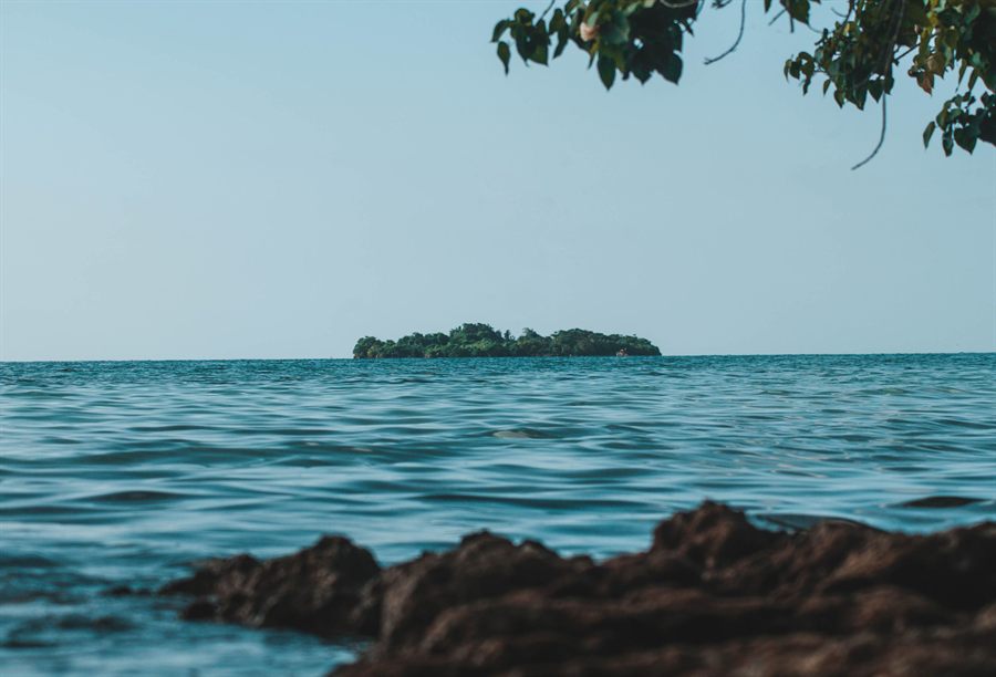 Small island on the horizon seen across the sea from a rocky Jamaican shore